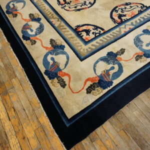 A cream and navy rug with crane and cloud medallions lies on worn wooden floorboards.