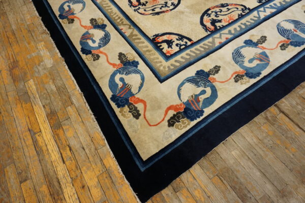 A cream and navy rug with crane and cloud medallions lies on worn wooden floorboards.