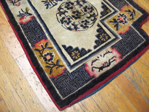 Cream rug corner with navy, gold, and red traditional patterns lies on distressed wood planks.