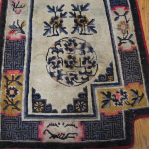 Worn cream, blue, and gold rug featuring a medallion and stepped geometric borders on hardwood flooring.