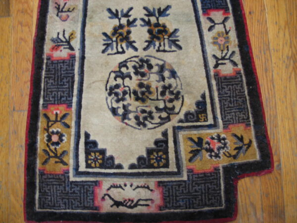 Worn cream, blue, and gold rug featuring a medallion and stepped geometric borders on hardwood flooring.