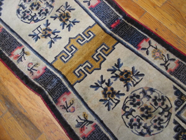Cream rug runner featuring blue floral sprays and a wide gold geometric pattern against wood floors.