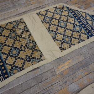 A salvaged textile with blue and tan geometric diamond patterns and borders rests on distressed wood planks.