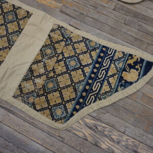 Segmented blue and gold low-pile runner with wide beige fabric trim rests on rustic wooden planks.