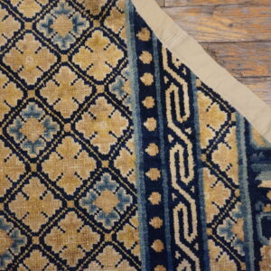 Navy and gold geometric patterned rug section showing a fabric binding on rustic wood planks.