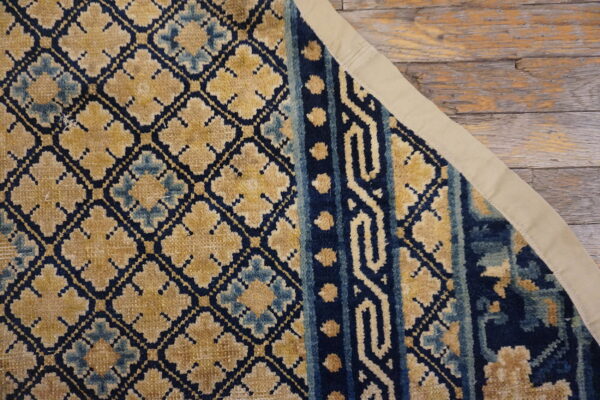 Navy and gold geometric patterned rug section showing a fabric binding on rustic wood planks.