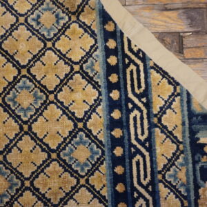 Detail view of a navy, gold, and light blue patterned rug on distressed wooden planks.