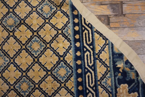 Detail view of a navy, gold, and light blue patterned rug on distressed wooden planks.