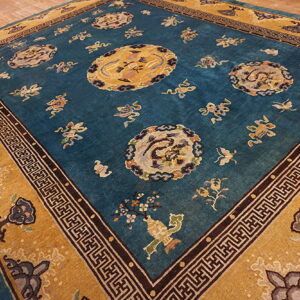 Ornate teal and mustard yellow rug with dragon motifs and black geometric borders rests on wood floorboards.