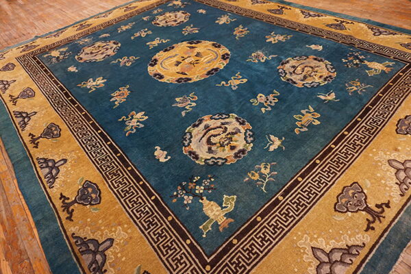 Ornate teal and mustard yellow rug with dragon motifs and black geometric borders rests on wood floorboards.