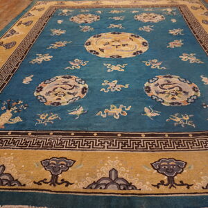 A large teal rug with central medallions and a gold border rests on natural wood plank flooring.