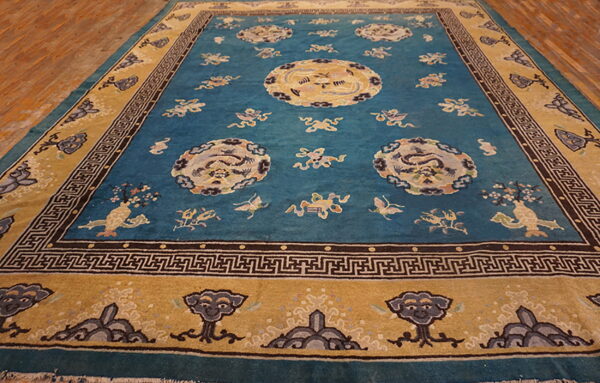 A large teal rug with central medallions and a gold border rests on natural wood plank flooring.