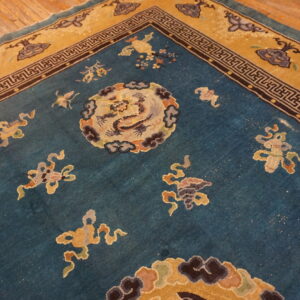 Teal and mustard low-pile rug with geometric and mythological patterns resting on rustic wooden floorboards.