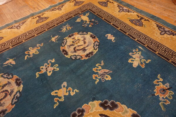 Teal and mustard low-pile rug with geometric and mythological patterns resting on rustic wooden floorboards.