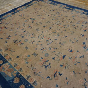 Low-pile tan rug featuring scattered blue and peach floral designs, bordered in wide dark navy blue on wood.