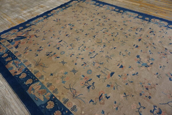 Low-pile tan rug featuring scattered blue and peach floral designs, bordered in wide dark navy blue on wood.
