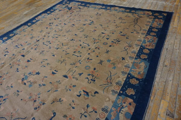 Beige rug featuring scattered blue and peach motifs, bordered in dark navy blue, placed on wood plank floors.