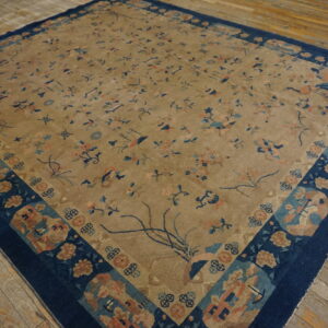 Large beige rug with sparse blue and pink motifs and a thick navy border on distressed wood flooring.