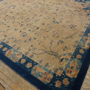 Beige rug with subtle blue and peach patterns and a deep blue ornate border on worn wood floors.