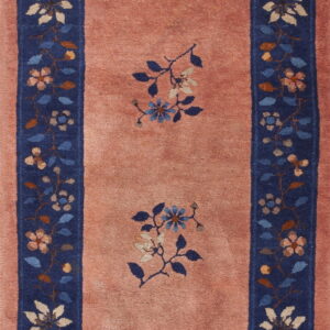 A rose pink rug with a navy blue border featuring multicolored floral designs and two central medallions.