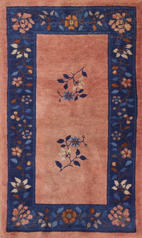 A rose pink rug with a navy blue border featuring multicolored floral designs and two central medallions.