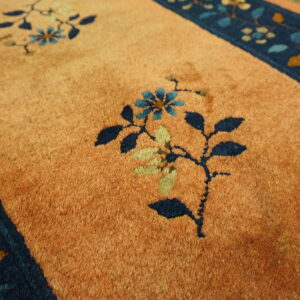 Orange cut-pile rug with dark blue borders and stylized floral patterns in blue, green, and gold.