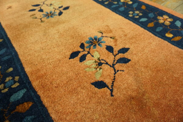 Orange cut-pile rug with dark blue borders and stylized floral patterns in blue, green, and gold.