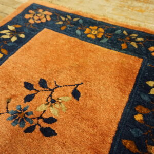 Rust-colored rug field with navy and gold floral border detail shown on distressed wood floor.