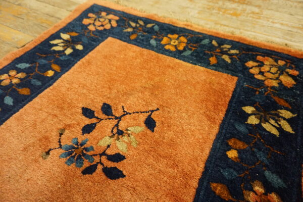 Rust-colored rug field with navy and gold floral border detail shown on distressed wood floor.