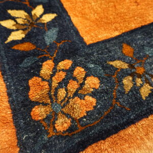 Close-up of a shaggy orange rug with a navy floral border on visible wood planks.