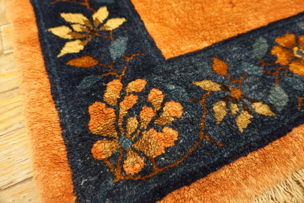 Close-up of a shaggy orange rug with a navy floral border on visible wood planks.