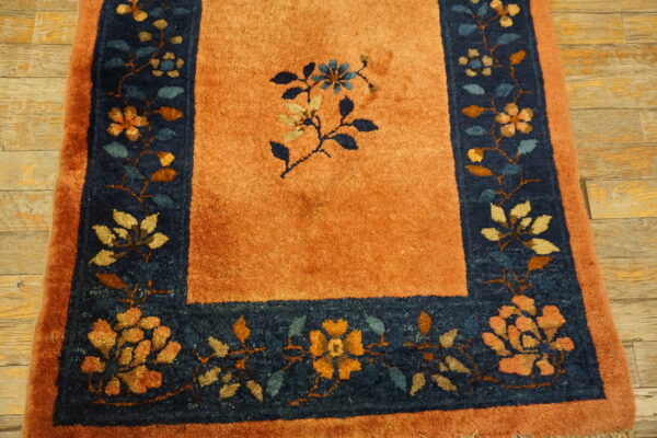 Rust-colored rug with a dark blue border featuring multicolored floral designs on distressed wood flooring.