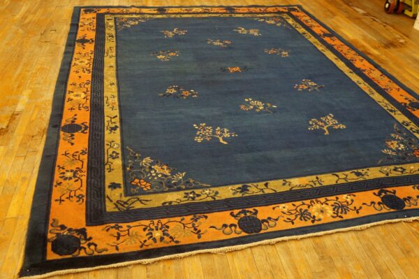 Blue area rug with sparse floral motifs, framed by wide orange and olive patterned borders on a light wood floor.