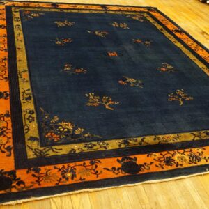 A navy rug with sparse floral motifs and an orange, gold, and blue border rests on hardwood flooring.