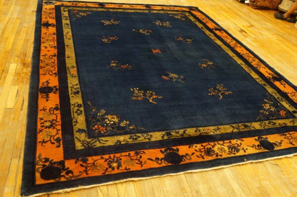 A navy rug with sparse floral motifs and an orange, gold, and blue border rests on hardwood flooring.