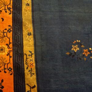 Deep blue rug with sparse floral designs and wide orange and gold striped borders on wood flooring.