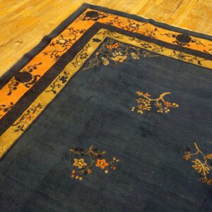 Navy blue rug features gold and orange floral patterns and borders on a bright wood plank floor.