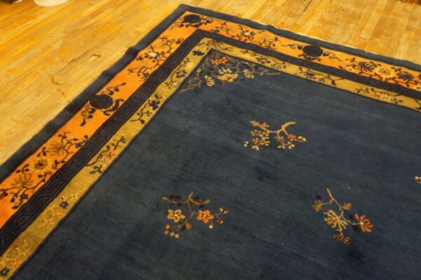 Navy blue rug features gold and orange floral patterns and borders on a bright wood plank floor.