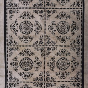 Low-pile rug with black repeating medallion and fretwork patterns on a light beige rectangular grid.