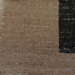 Close-up detail of a tan flatweave rug with a contrasting black geometric border pattern.