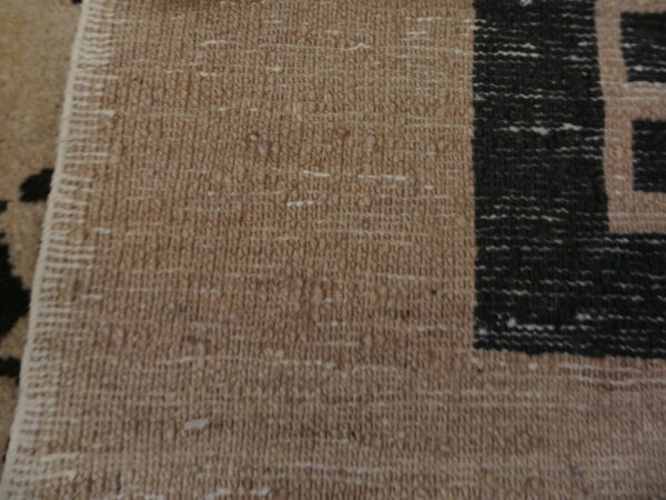 Close-up detail of a tan flatweave rug with a contrasting black geometric border pattern.