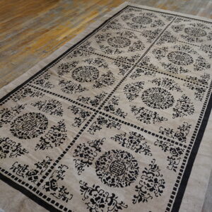 Beige rug with a contrasting black repeating medallion and lattice pattern rests on hardwood floorboards.