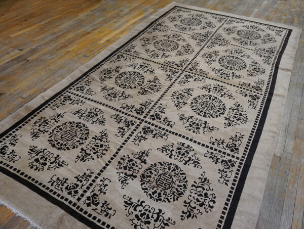 Beige rug with a contrasting black repeating medallion and lattice pattern rests on hardwood floorboards.