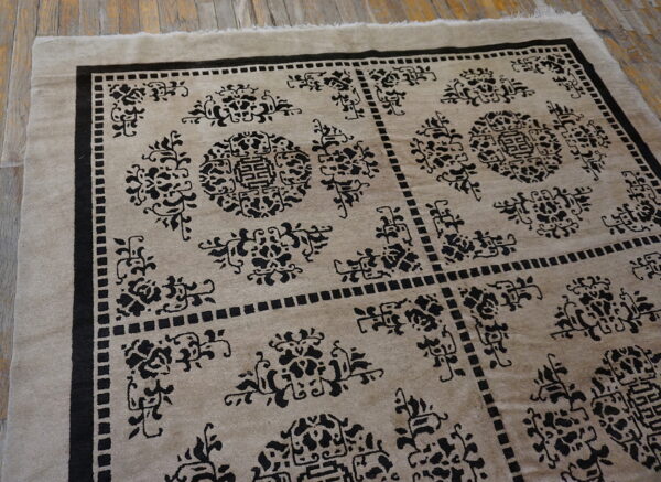 Taupe rug featuring dense black geometric and stylized floral motifs lies on weathered wood flooring.