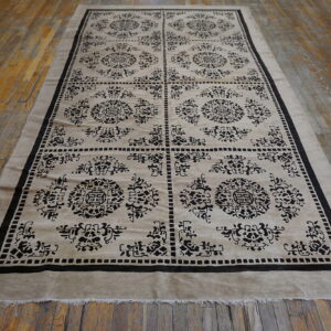 Low pile beige and black rug with boxed medallions and trellis patterns on rustic wood flooring.