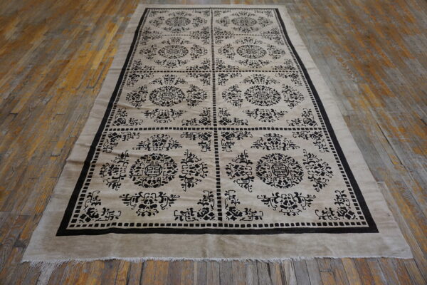 Low pile beige and black rug with boxed medallions and trellis patterns on rustic wood flooring.