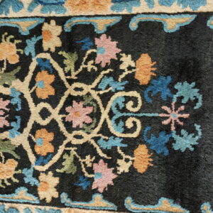 Detailed view of a rug's dark field and beige border featuring pink, blue, and orange florals.