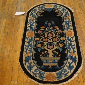 Oval black rug with stylized floral designs in blue, tan, and orange on distressed wood flooring.