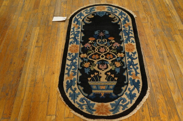 Oval black rug with stylized floral designs in blue, tan, and orange on distressed wood flooring.