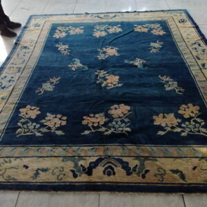 Blue field rug with floral motifs and a pale gold patterned border lying on glossy white tile floor.